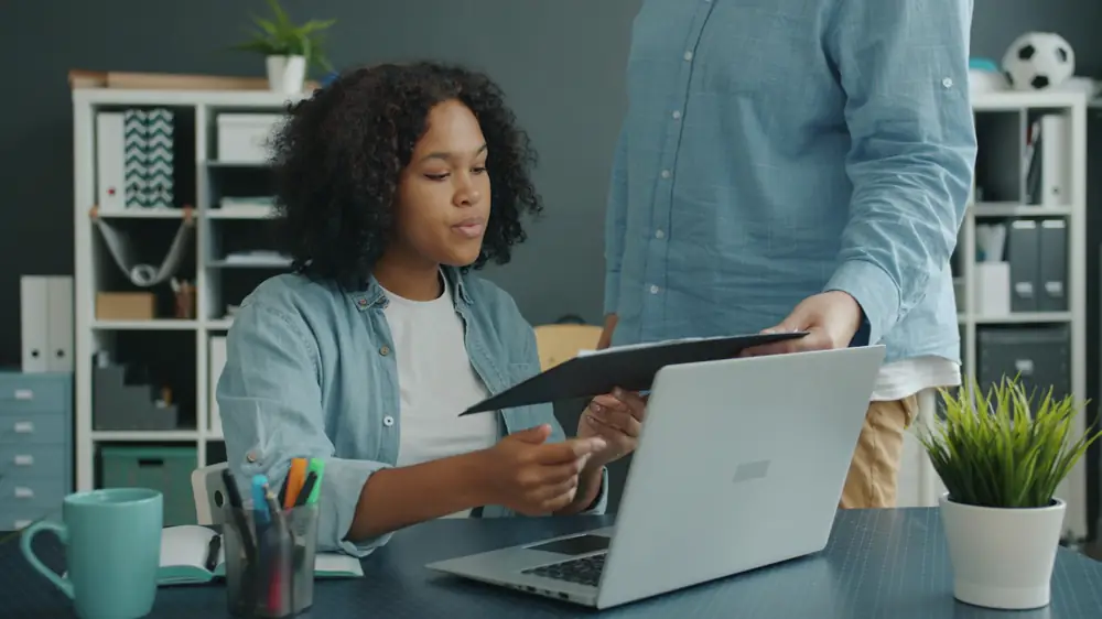 A colleague handing an HR officer a printed CV at her desk